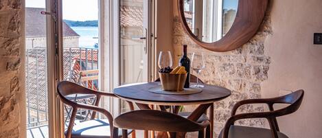 Un área de comedor con una mesa redonda, dos sillas, un cuenco de uvas y una botella de vino.