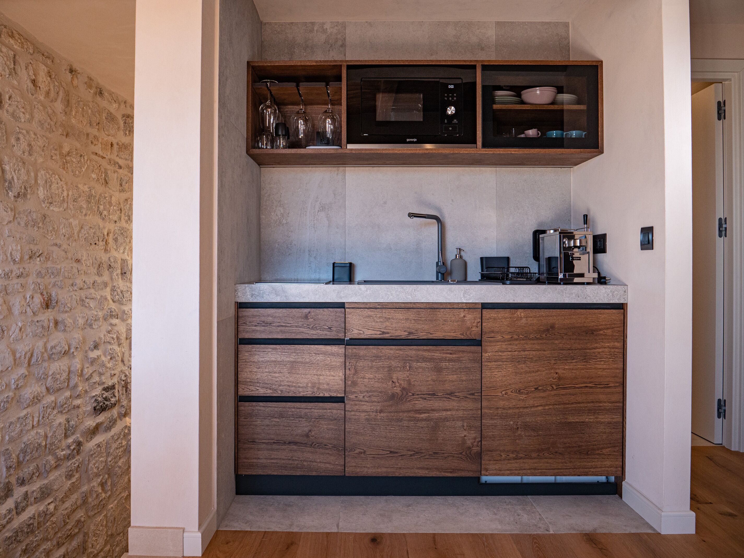 Una cocina moderna con pared de piedra, armarios de madera, microondas integrado y cafetera.