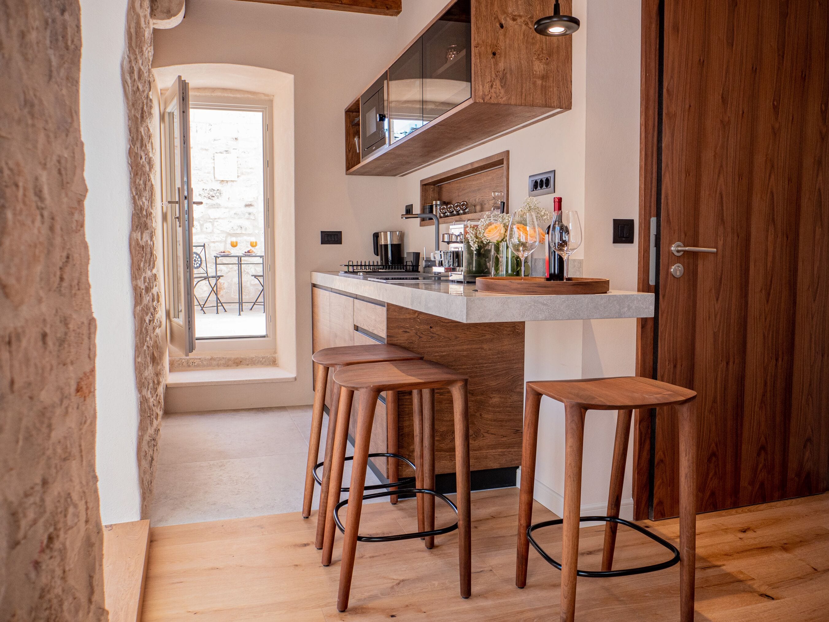 A modern kitchen with wooden stools, a built-in bar, and a view to the outside.