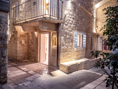 A stone building with a balcony, a door, and a window with shutters.