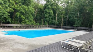 Una piscina rectangular con cubierta de madera y sillas de descanso.