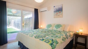 Ein Schlafzimmer mit Bett, Nachttisch, Wand-Klimaanlage und einem Bild von einer Strandlandschaft.
