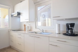 Una cocina moderna con gabinetes blancos, un lavamanos de acero inoxidable y una cafetera.