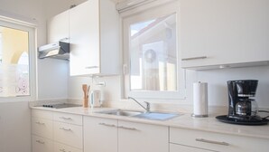 Eine Küche mit weißen Schränken, einer Edelstahlspüle, einer Kaffeemaschine und einem Fenster mit Jalousien.
