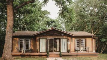 Une cabane en bois dotée d’une véranda, de grandes fenêtres et d’un petit jardin devant.
