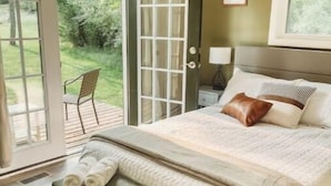 A bedroom with a bed, a bench, a nightstand, a lamp, and a door leading to a balcony. - Cottage near water park, golf and skiing at Massanutten Resort! (McGaheysville)