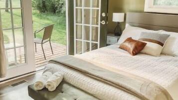 Une chambre à coucher comprenant un lit, un banc, une table de chevet, une lampe et une porte donnant sur un balcon.