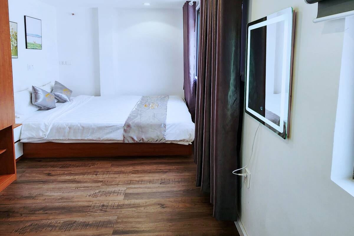 A narrow room with a bed, wooden flooring, a window, and a wall-mounted TV.