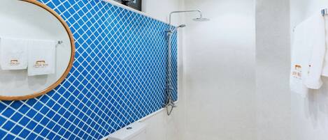 Un baño con pared de azulejos azules, un lavamanos blanco, un inodoro y una ducha.
