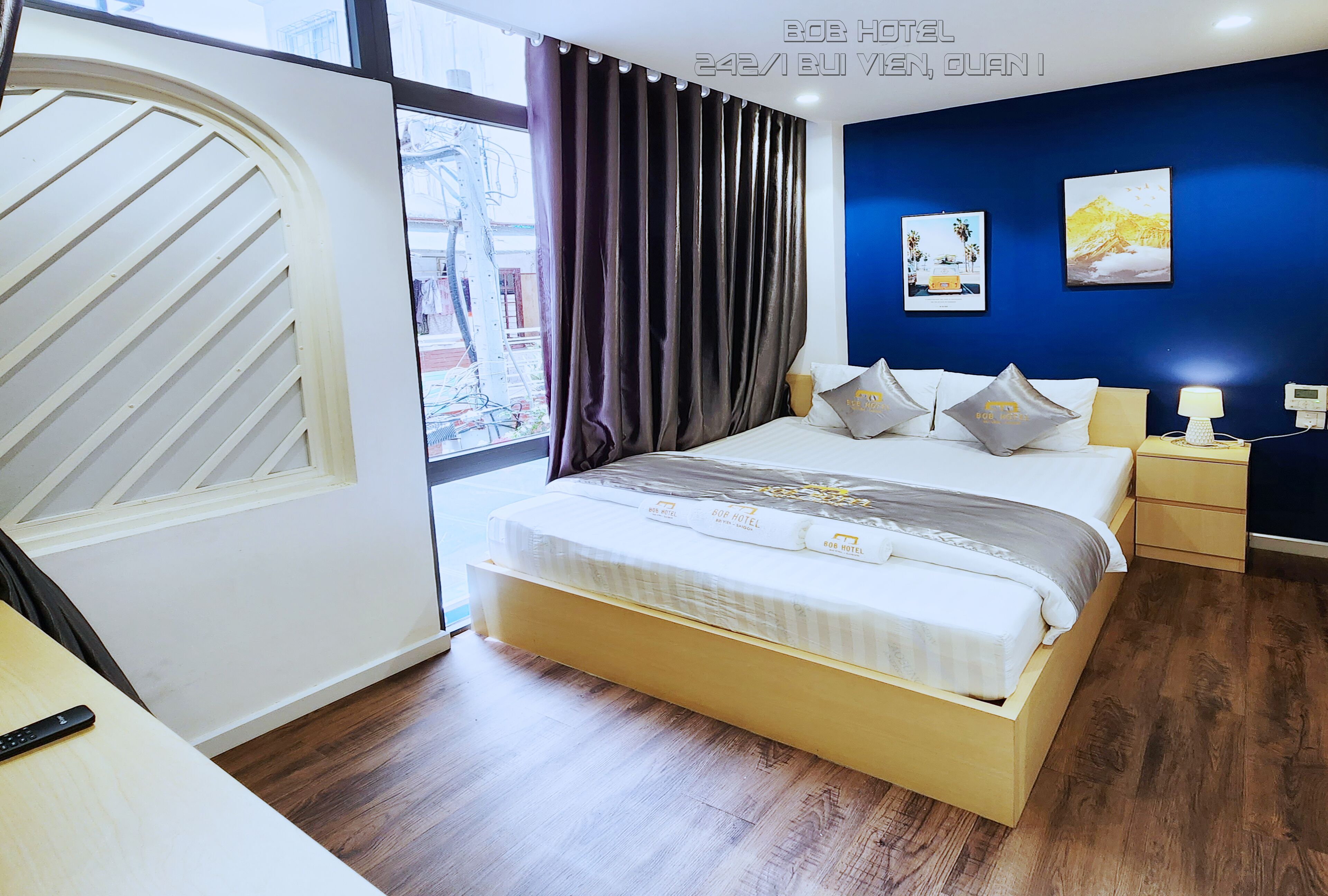 Une chambre d’hôtel avec un lit, une table de chevet, une lampe et une fenêtre avec des rideaux.