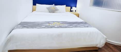 A neatly made bed with a white and gray bedspread, a wooden headboard, and a nightstand with a lamp.