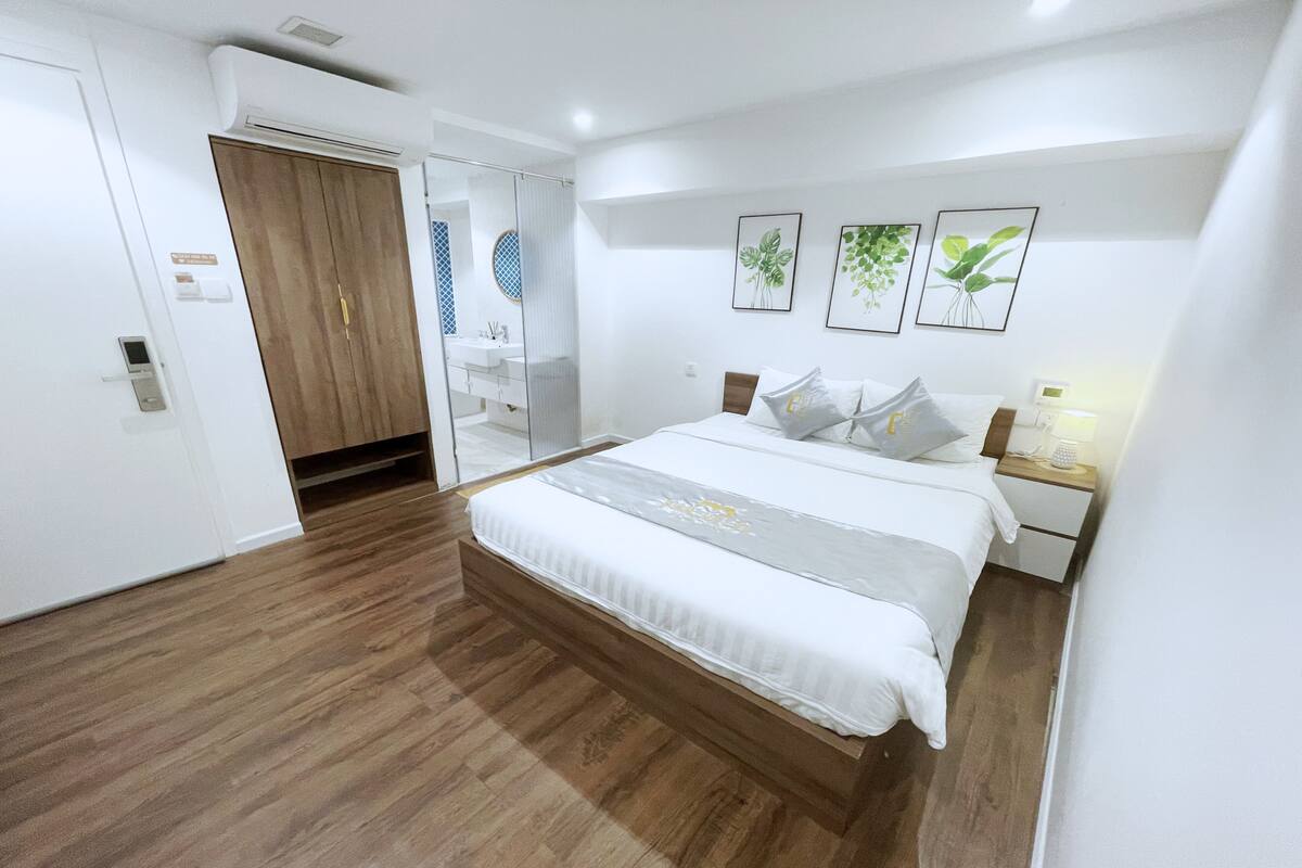 A modern bedroom with a wooden floor, a bed with white bedding, a nightstand, and wall-mounted artwork.