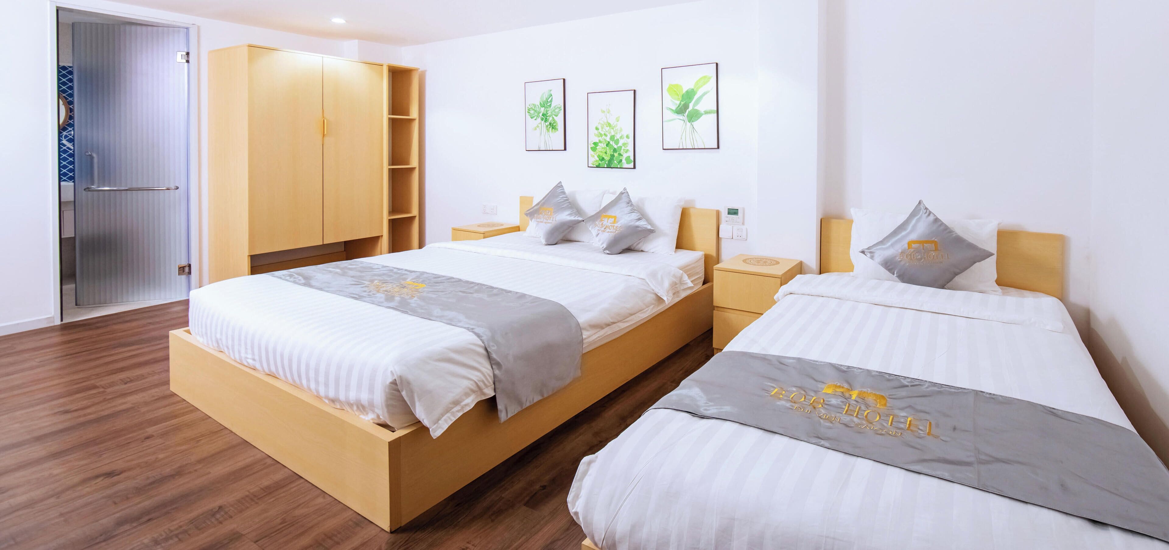 A hotel room with two beds, a wardrobe, a bedside table, a nightstand, and wall art.