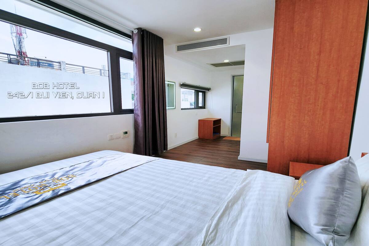 A hotel room with a bed, a window with a view, a wooden floor, and a door leading to another room.