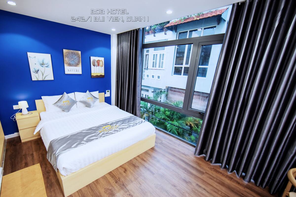 A hotel room with a large bed, bedside tables, and a view of greenery outside.