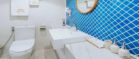A bathroom with a toilet, sink, and mirror. The walls are tiled in blue and white.