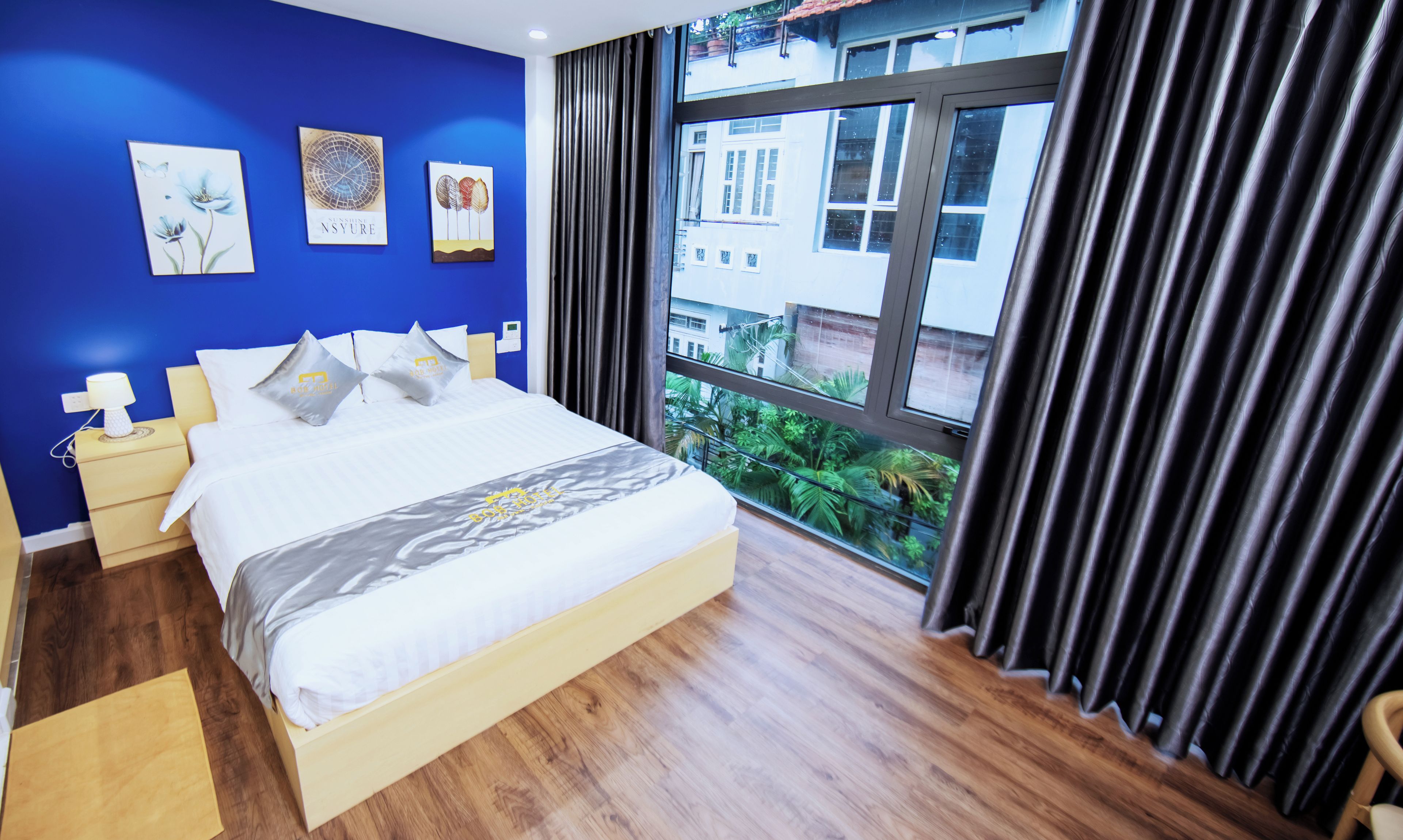 A hotel room with a large bed, bedside tables, and a view of greenery outside.