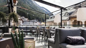 A rooftop terrace with outdoor seating, a view of a mountain, and traditional architecture in the background. - Goldener Adler (Ischgl)