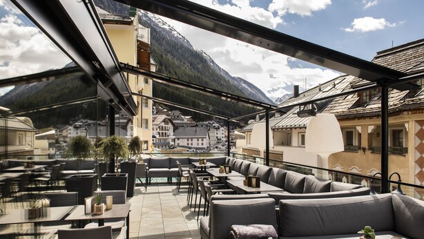 Een terras met tafels en banken, met uitzicht op een bergachtig landschap.