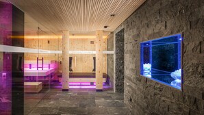 A spa area with wooden paneling, stone walls, and a large aquarium window. - Goldener Adler (Ischgl)