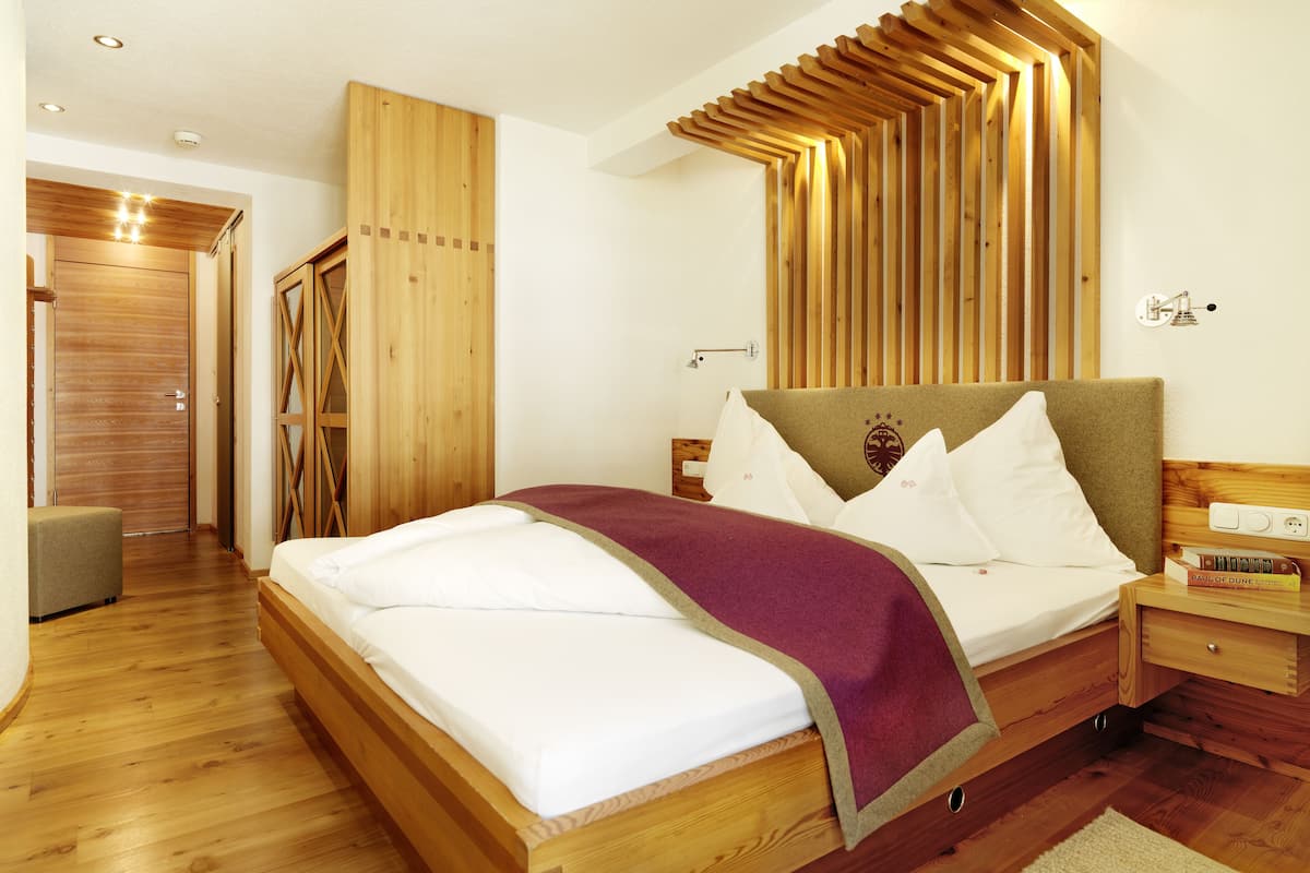 Un dormitorio con estructura de cama de madera, cabecera con listones verticales, mesita de noche con lámpara y armario con puerta de espejo.