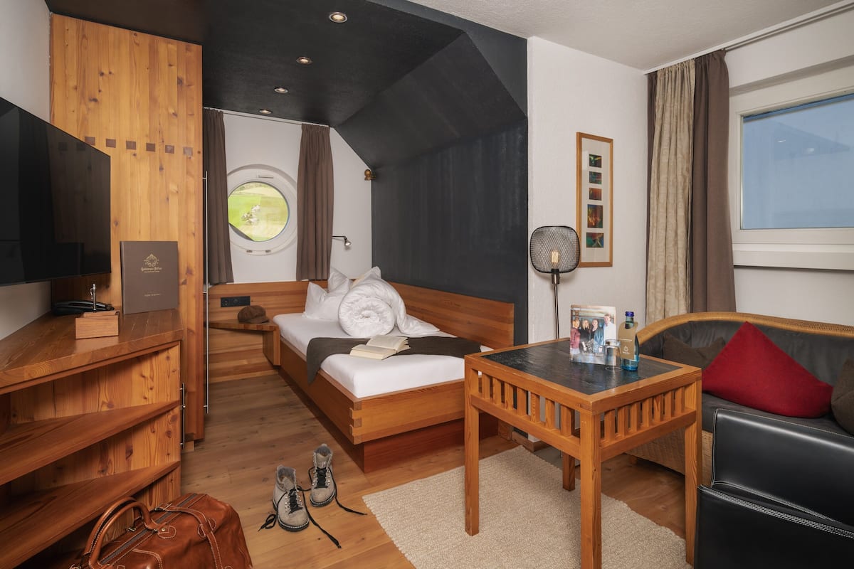 Una habitación de hotel con una cama, un escritorio de madera, un sofá, un ventanal redondo y un ventilador de techo.