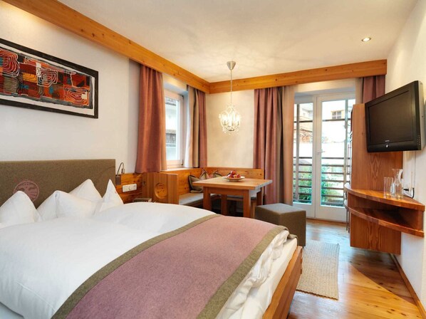 Una habitación de hotel con una cama grande, un banco de madera, una mesa de comedor y una televisión.