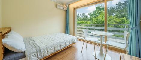 A bedroom with a bed, a small table, and chairs, a balcony with a railing, and a view of greenery outside.