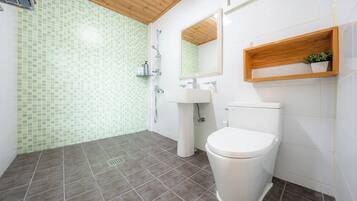 A bathroom with a shower, toilet, sink, and a wooden shelf with a plant.
