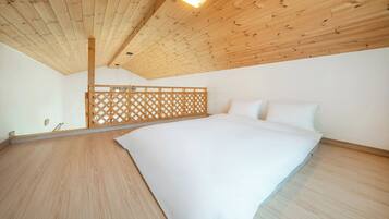 A bedroom with a wooden ceiling, a bed with white bedding, and a wooden floor.