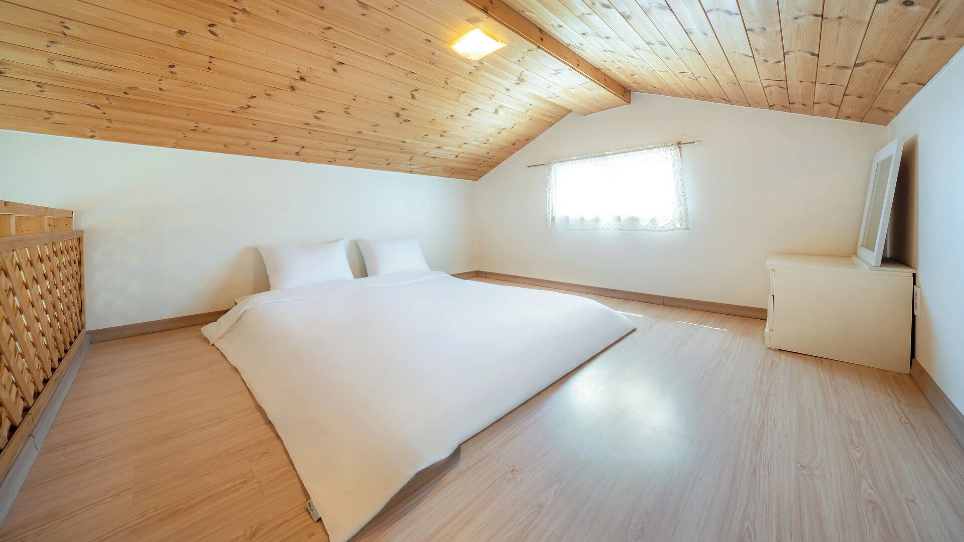 A bedroom with a wooden ceiling, a bed, a window, and a small bedside table.