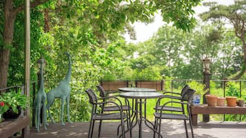 Una terraza de madera con una mesa redonda y cuatro sillas, rodeada de follaje y una estatua de jirafa.