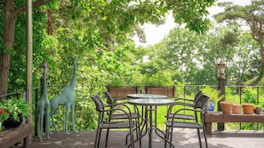 A wooden deck with a round table and four chairs, surrounded by greenery and a giraffe statue. - Ganghwado Elinhuvert Pension (Incheon)