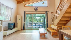 Una habitación con televisión, una banca, una mesa, una escalera y vistas al exterior.
