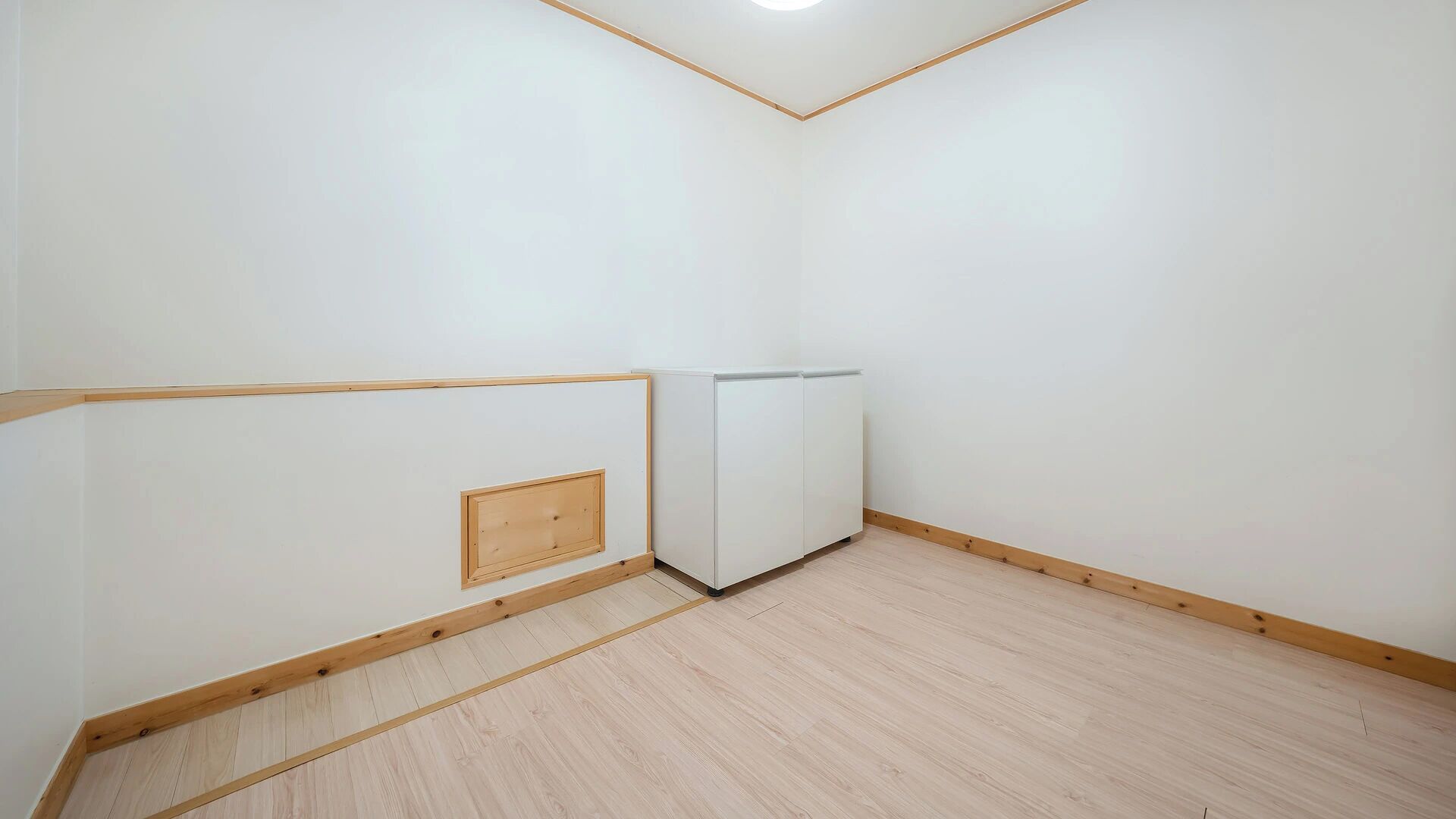 Una habitación con piso de madera, paredes blancas y un armario de esquina.