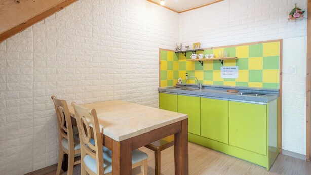 Eine kleine Küchenzeile mit Holztisch und -stühlen, einem Spülbecken und einer gefliesten Rückwand.