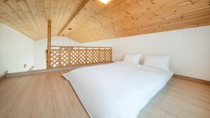 Ett sovrum med ett träpanelat tak, en säng med vita sängkläder och ett trägolv.