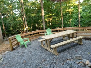 Zona de picnic con una mesa de madera y bancos, rodeada de grava y árboles.
