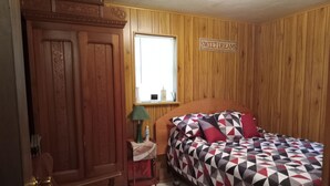 Ein Schlafzimmer mit einem Holzschrank, einem Nachttisch mit Lampe, einem Bett mit gemustertem Bettbezug und einem Fenster mit der Aufschrift 'SWEET DREAMS'.