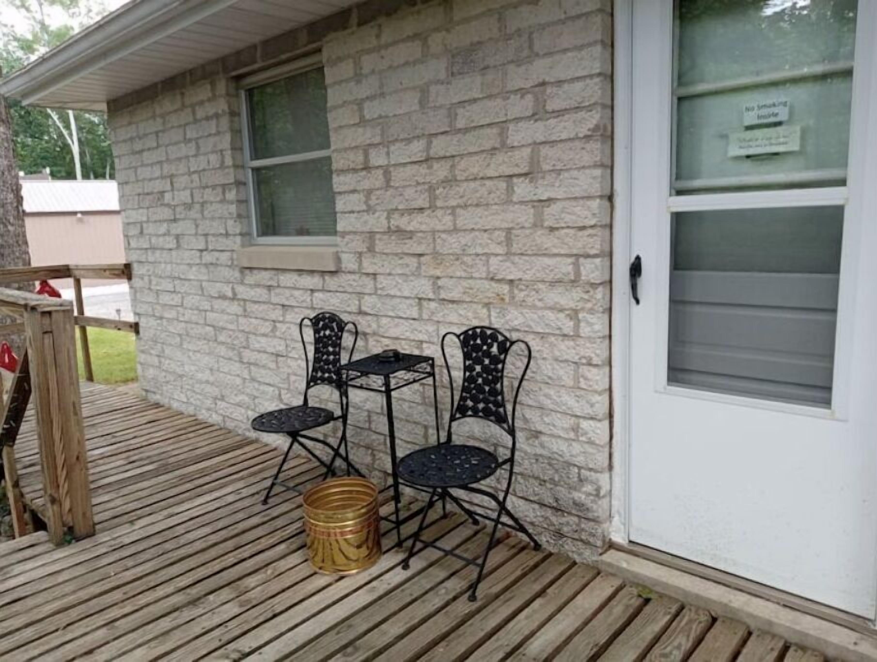 Una casa con fachada de ladrillo, una terraza de madera, dos sillas de metal y una pequeña mesa.