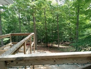 A wooden deck with a simple railing, surrounded by a forested area.