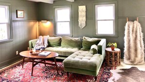 A cozy room with a green sofa, a round wooden coffee table, and a patterned rug. - Quaint & Cozy 1830s Cape- Central Location! (Wiscasset)