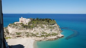 A coastal building with a white facade, situated on a rocky outcrop with a beach in the foreground and the sea in the background. - Blu Tropea Maison (Tropea)