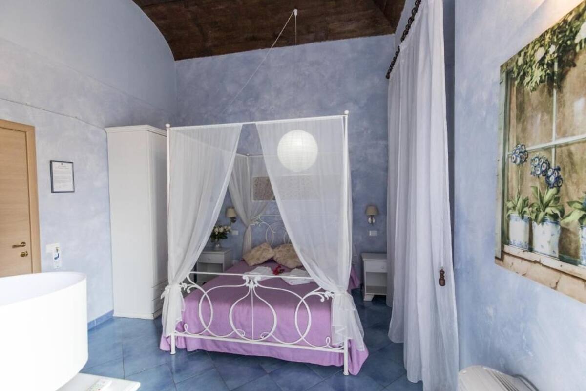 A bedroom with a four-poster bed, a white canopy, a wooden door, a white wardrobe, and a window with a plant.