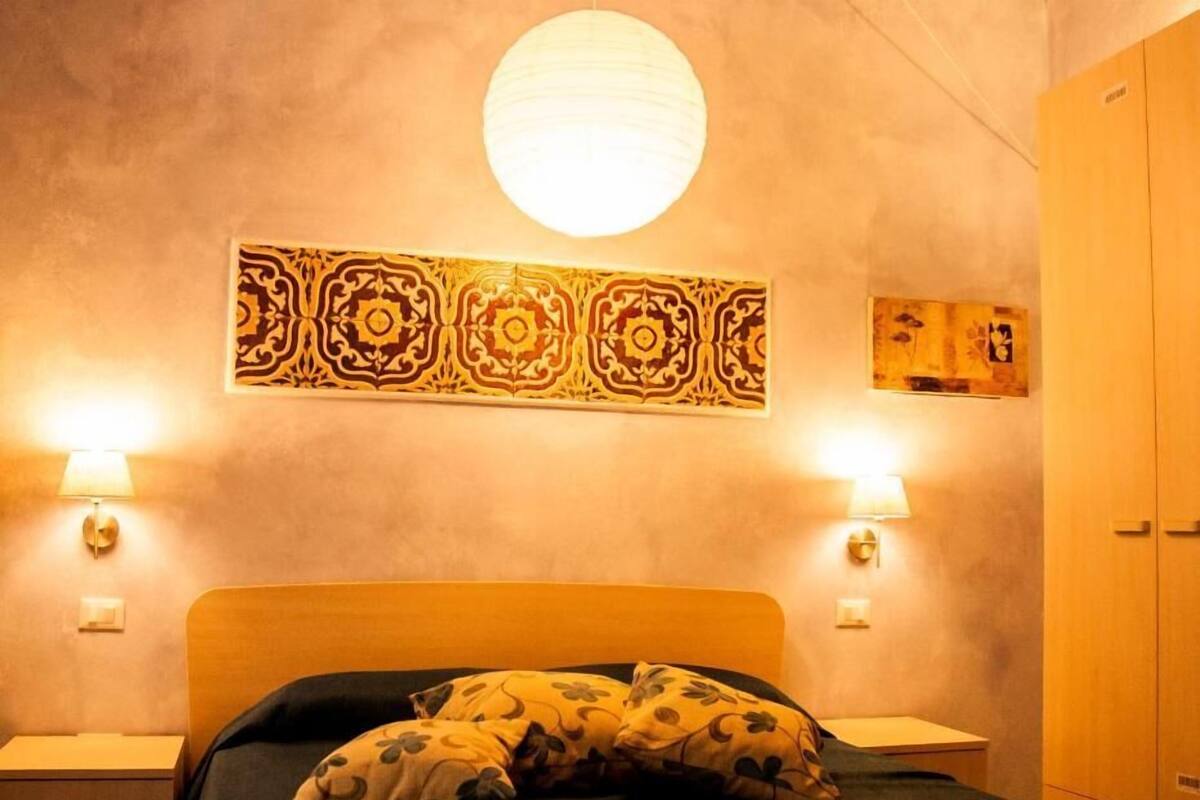 A bedroom with a bed, two bedside lamps, a wall tapestry, and a wardrobe.