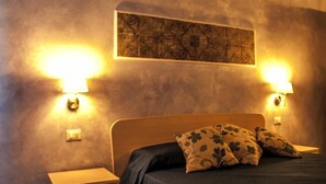 Quarto com cama, duas luminárias de cabeceira, mesa de cabeceira e uma obra de arte pendurada na parede.