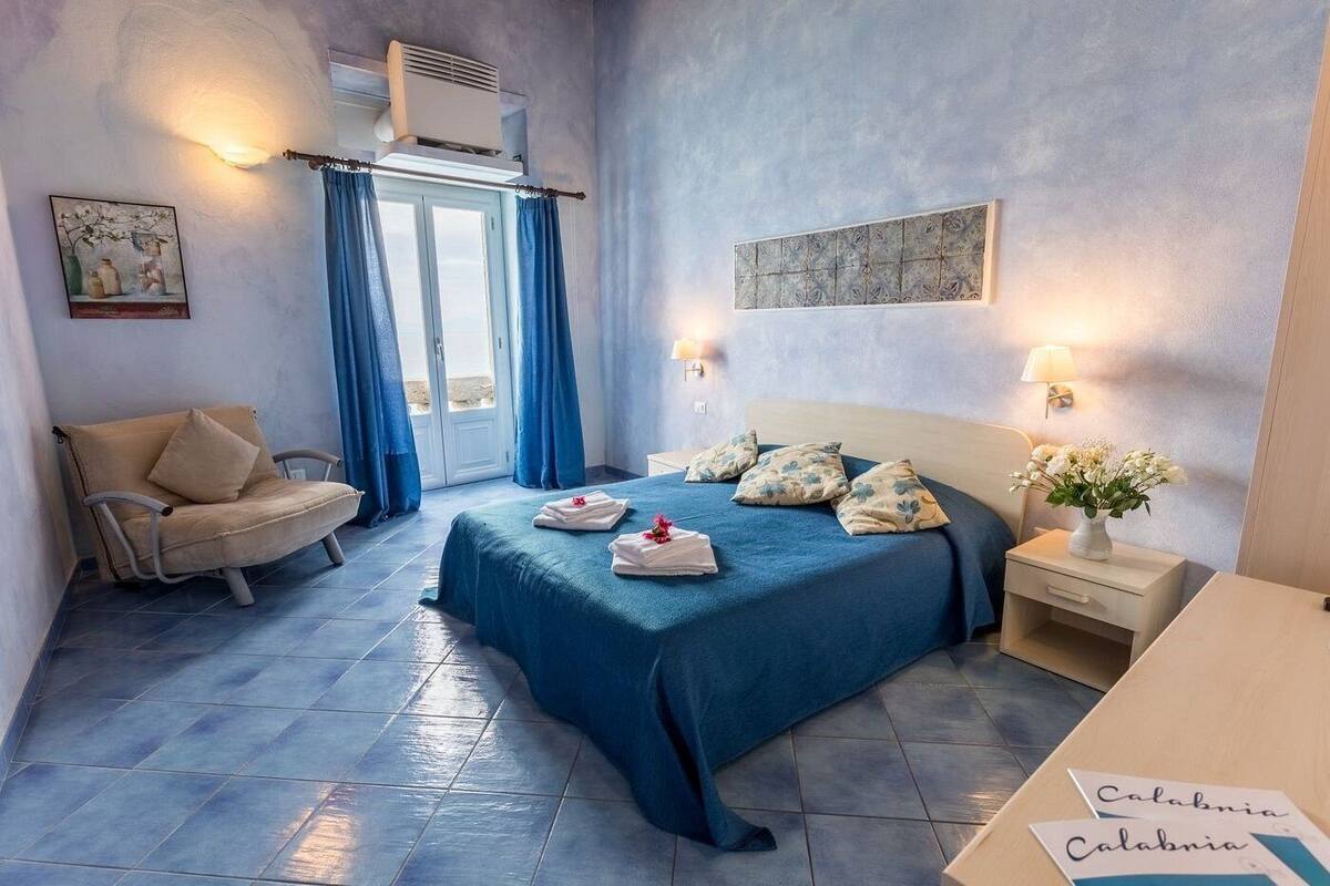 A bedroom with a bed, a chair, a nightstand, and a wall-mounted air conditioner.
