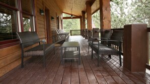 Een overdekt terras met houten vloer, metalen stoelen, een tafel en een vlag.