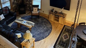 Een gezellige woonkamer met een stenen muur, een open haard, een groot raam, een televisie en een schommelstoel.