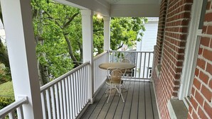 A covered porch with a table and chairs, white railings, and a brick wall. - Spacious restored 1914 historic home steps from the beach. (Cape Charles)